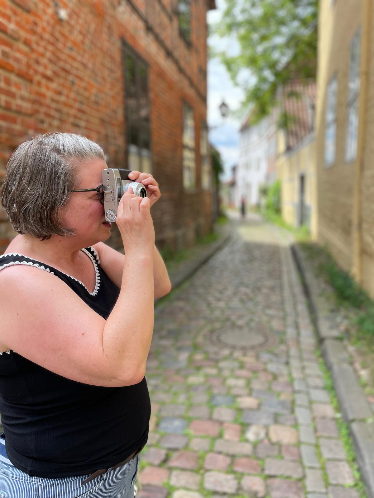 Teilnehmerin fotografiert mit einer kleinen analogen Kamera in einer historischen Gasse