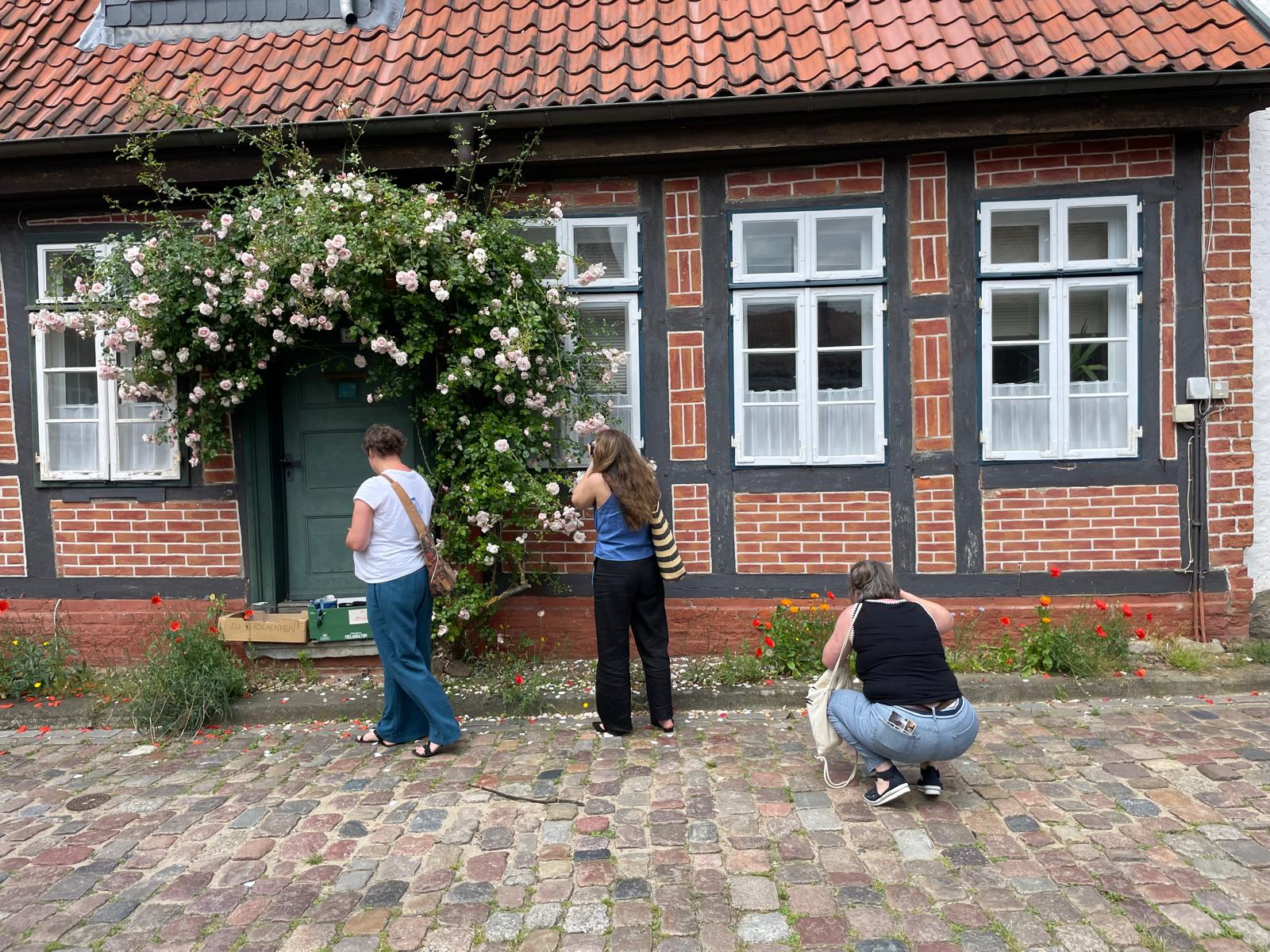 Drei Teilnehmende eines Firmenausflugs fotografieren ein Haus mit Rosen in Lüneburg