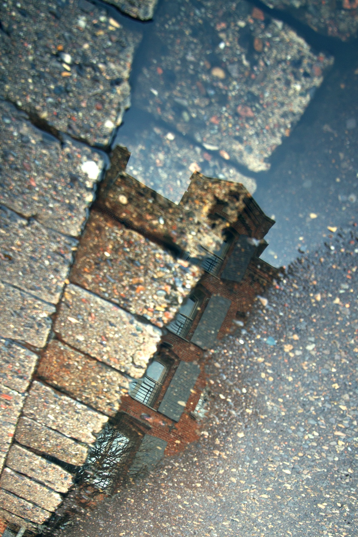 Pfütze mit Spiegelung von Backstein und Pflaster als Detailmotiv